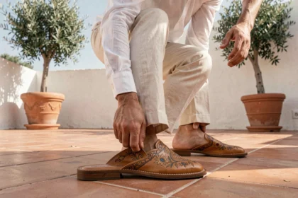 Homme élégant en lin crème enfilant une babouche en cuir artisanale sur une terrasse méditerranéenne ensoleillée